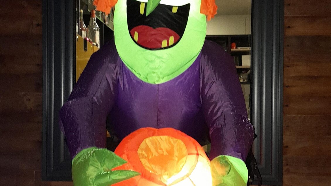 Eine leuchtende Halloween-Dekoration zeigt eine grüne Hexe mit lila Kleid und orangefarbenem Hut. Sie hält einen leuchtenden Kürbis in den Händen. | © Mountain Adventure Golf