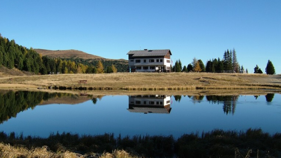 Ein idyllisches Haus am Ufer eines ruhigen Sees. Die Umgebung ist von Bäumen und sanften Hügeln umgeben und reflektiert wunderschön im Wasser. | © Andreas Wieser